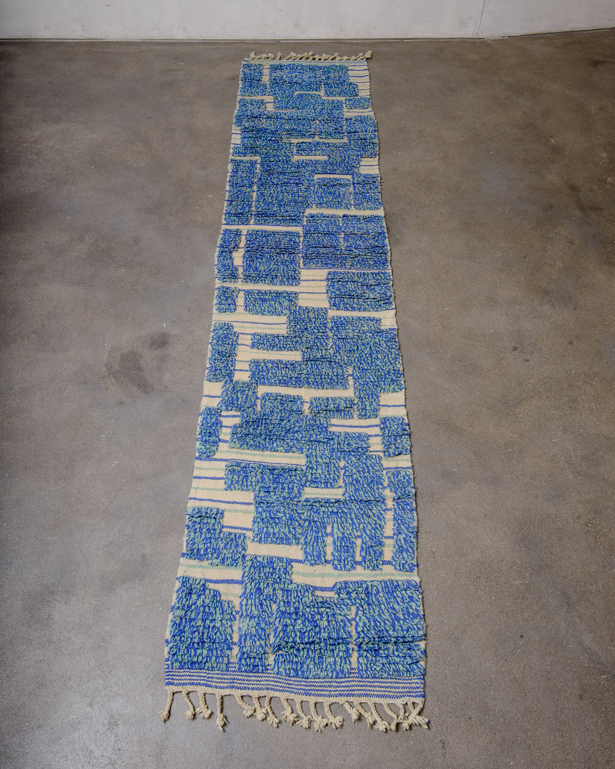 Berberlin vintage Berber runner rug made of blue and turquoise wool, laying flat on a concrete floor.